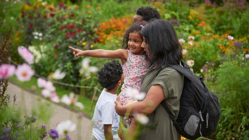 A young family in the garden with a child in arms pointing at a flower